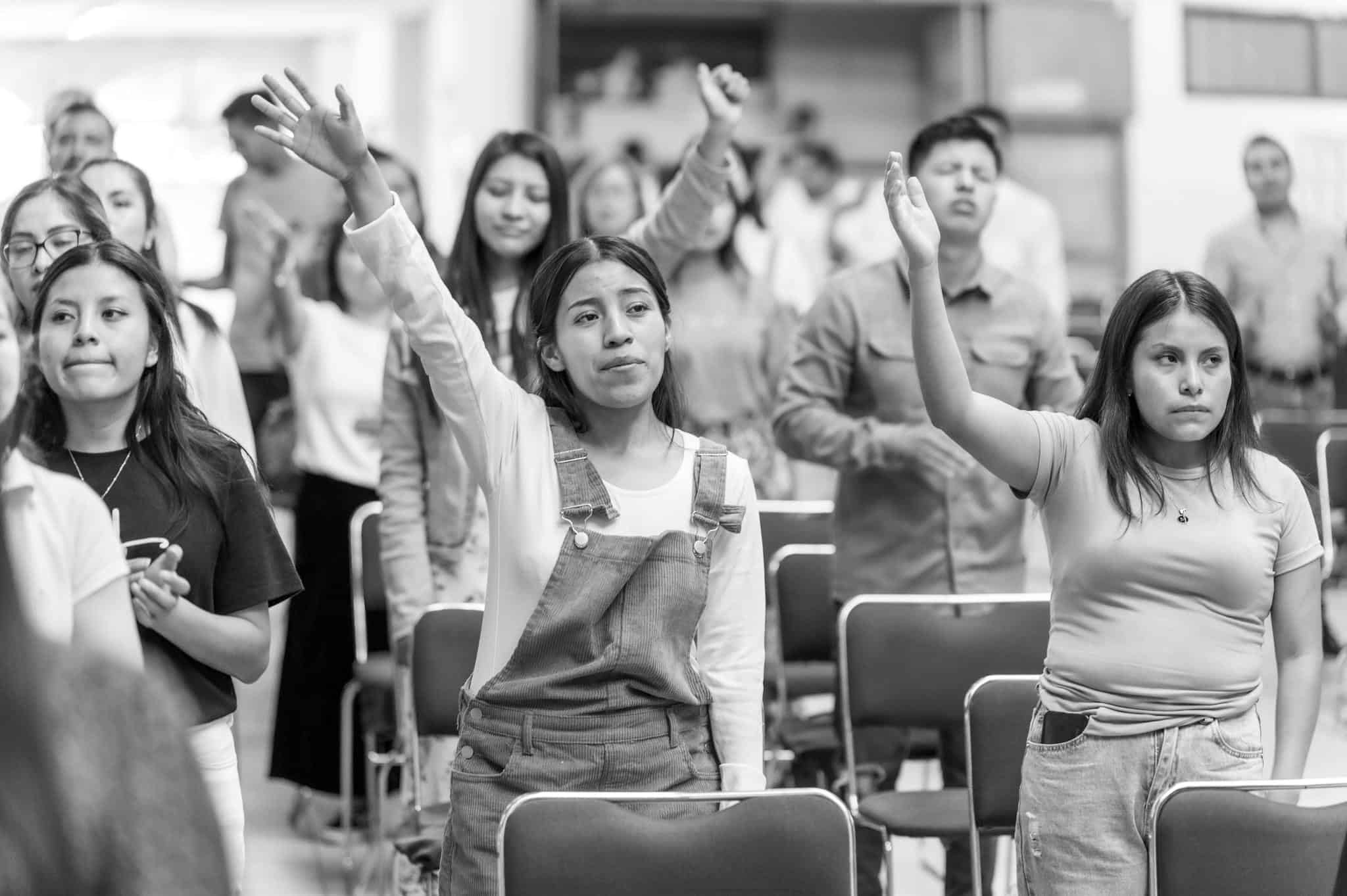 Young individuals in a worship gathering raising their arms in a church setting.